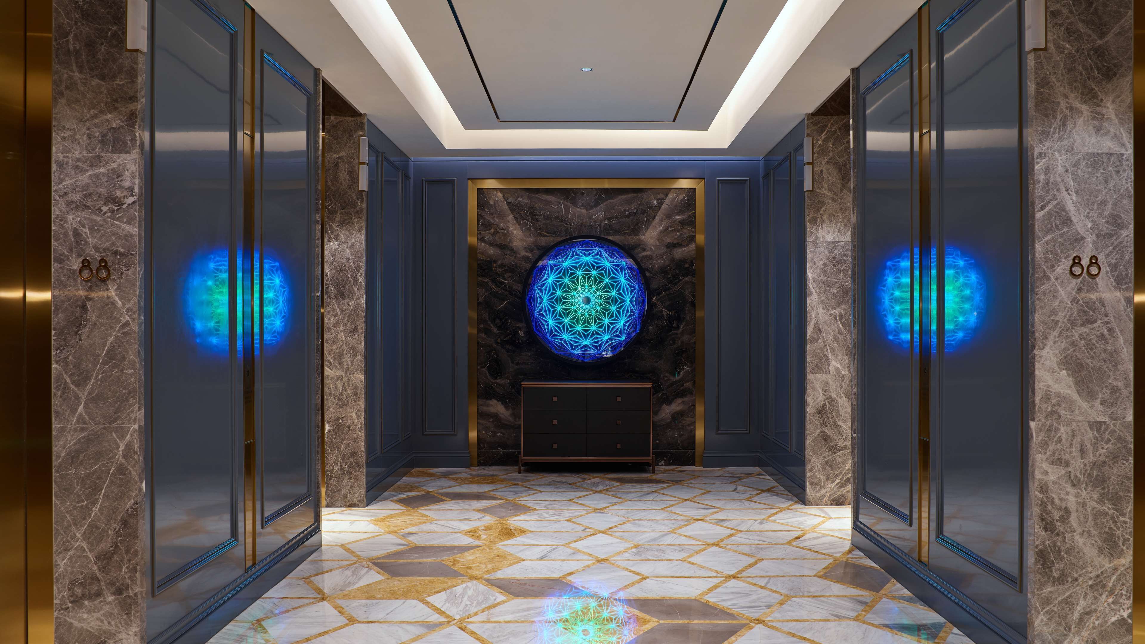 Interno di un ascensore moderno con pareti in marmo, pavimento a motivi geometrici e lampadario decorativo al centro.