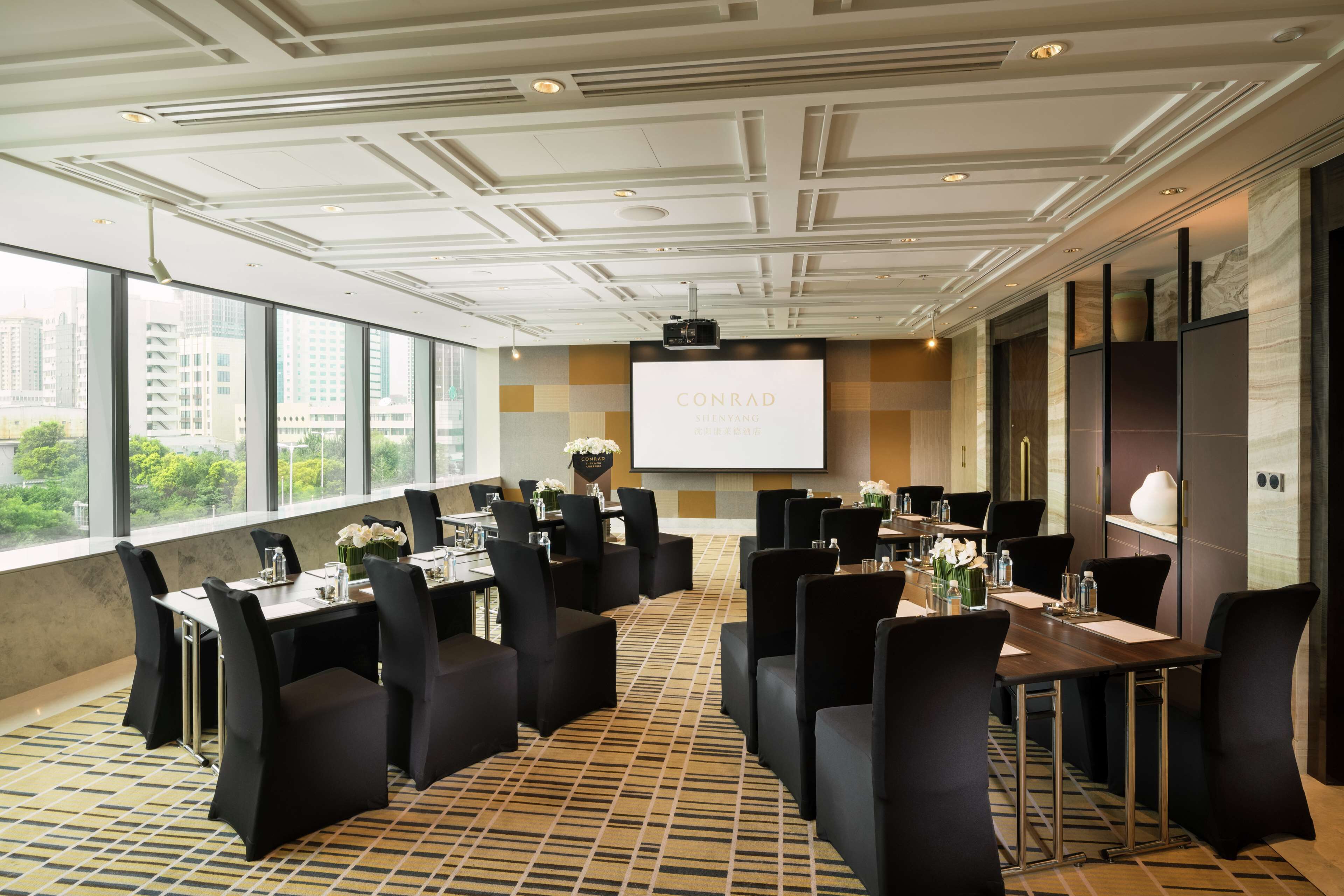 A conference room with a large screen displaying 'CONRAD SHENZHANG' and a city view through large windows.