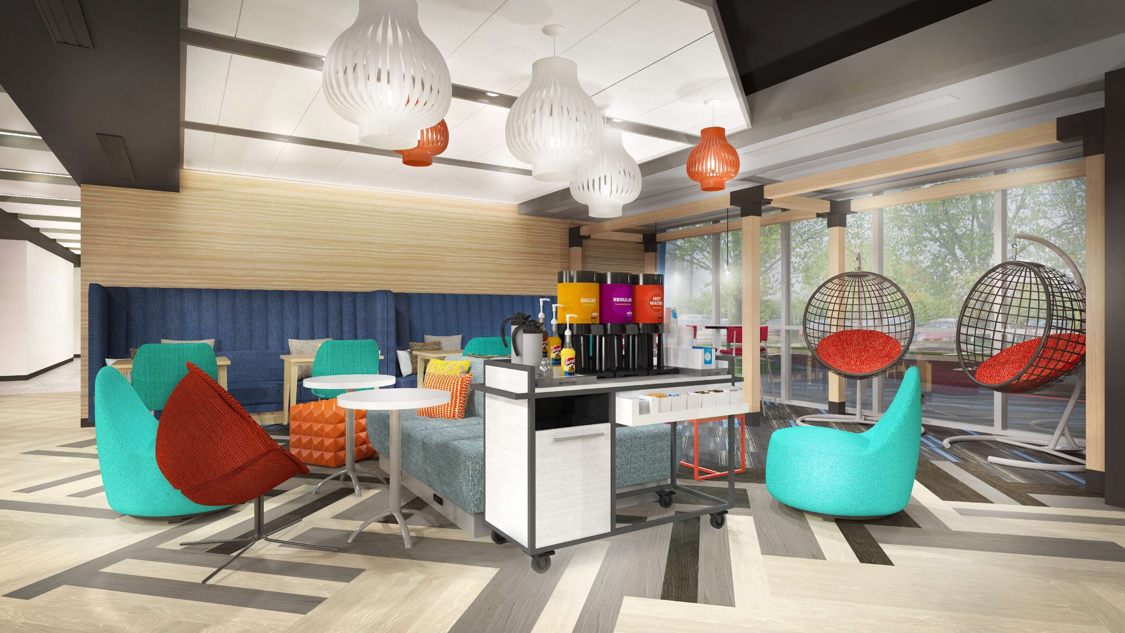 Un hall d'hôtel moderne, doté de sièges aux couleurs vives, d'un espace proposant des boissons en libre-service et de grandes fenêtres offrant une vue sur l'extérieur.