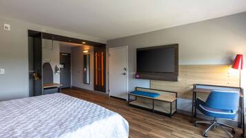 A hotel room with a bed, a desk with a chair, a TV mounted on the wall, and a bench.