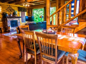 A cozy cabin interior with a stone fireplace, wooden dining table, and a staircase.
