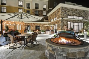 A courtyard with a fire pit, outdoor seating, and a covered area with string lights.