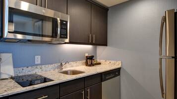 A modern kitchen with dark wood cabinets, stainless steel appliances, a marble countertop, and a built-in dishwasher.