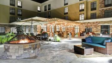 An outdoor patio area with a stone fire pit, seating, and a covered seating area with string lights.
