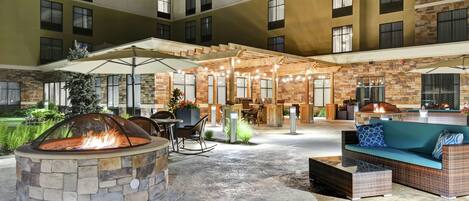 An outdoor patio area with a stone fire pit, seating, and a covered seating area with string lights.
