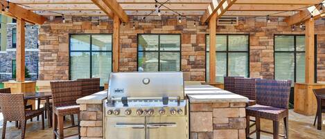 An outdoor barbecue area with a Weber grill, stone walls, wooden pergola, and wicker chairs.