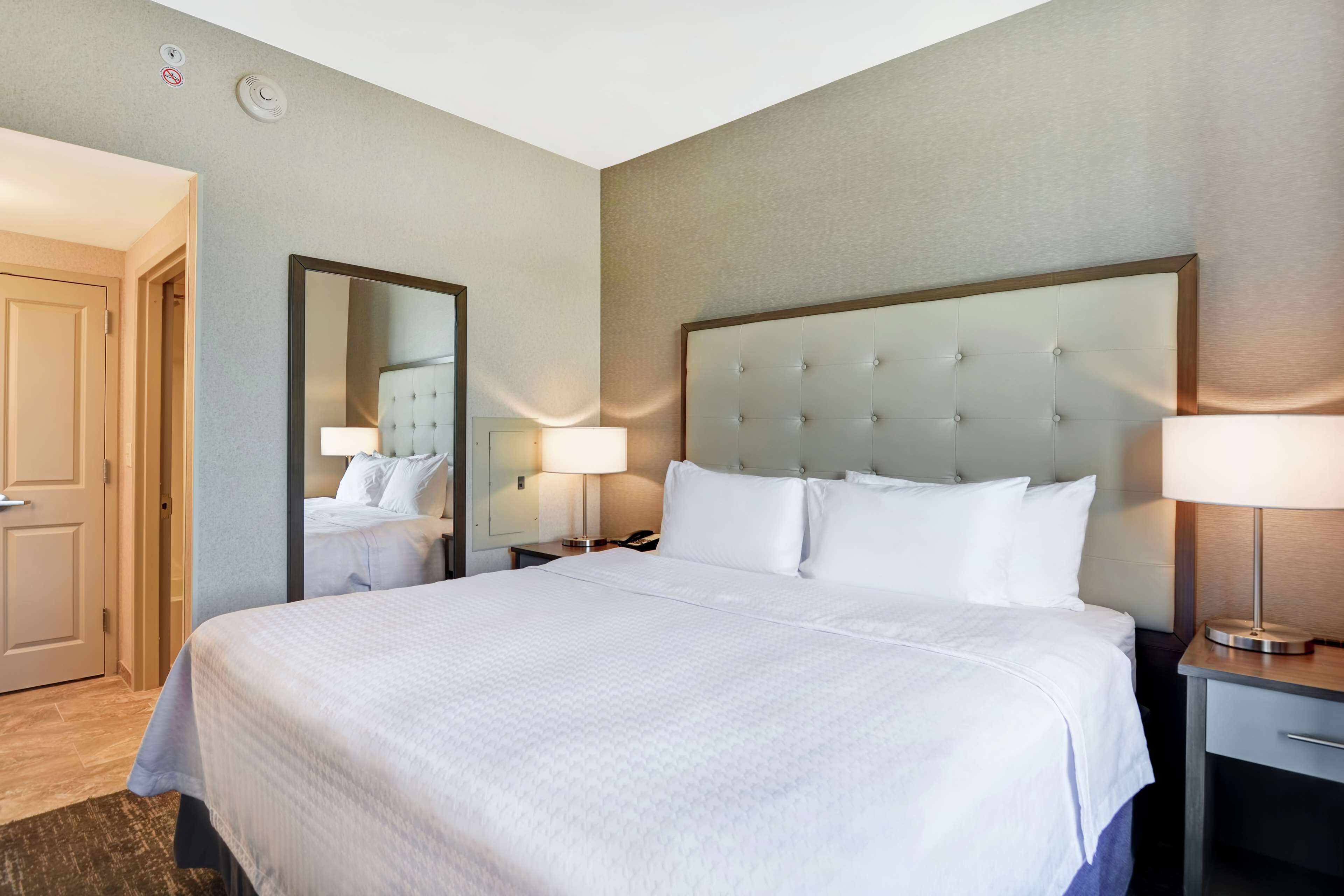 Een hotelkamer met een groot bed, een nachtkastje met een lamp, een spiegel en een deur.