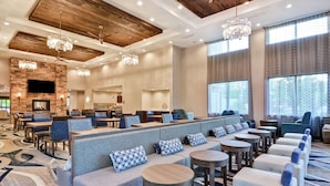 A spacious hotel lobby with a high ceiling, wooden beams, and a large seating area with sofas and round tables. - Homewood Suites by Hilton Poughkeepsie (Poughkeepsie)