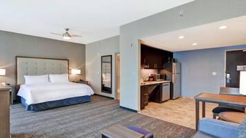 A hotel room with a bed, a desk, a kitchenette, and a seating area.