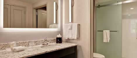 A modern bathroom with a marble sink, a large mirror, and a glass-enclosed shower.