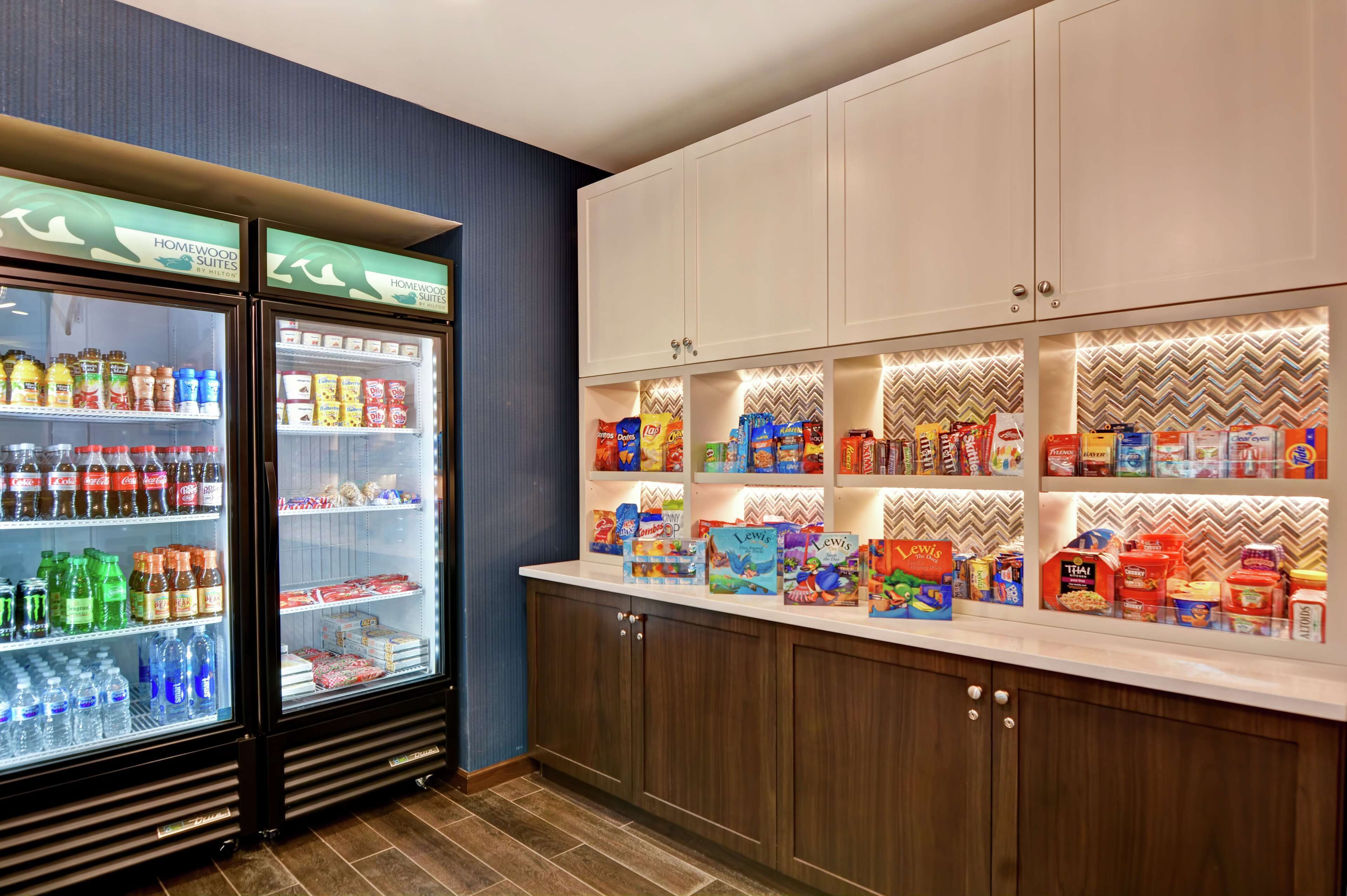 Una kitchenette con un refrigerador lleno de bebidas y aperitivos, un microondas y una cafetera.
