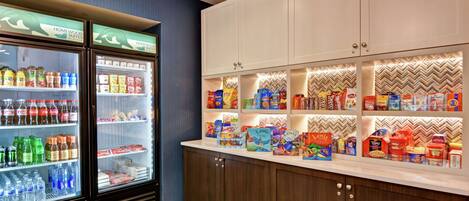 Una kitchenette con un refrigerador lleno de bebidas y aperitivos, un microondas y una cafetera.