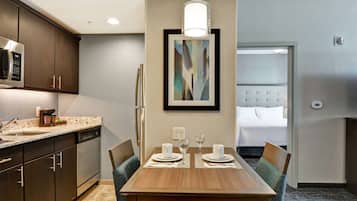 A modern hotel room with a dining area, kitchenette, and a bed with a tufted headboard.
