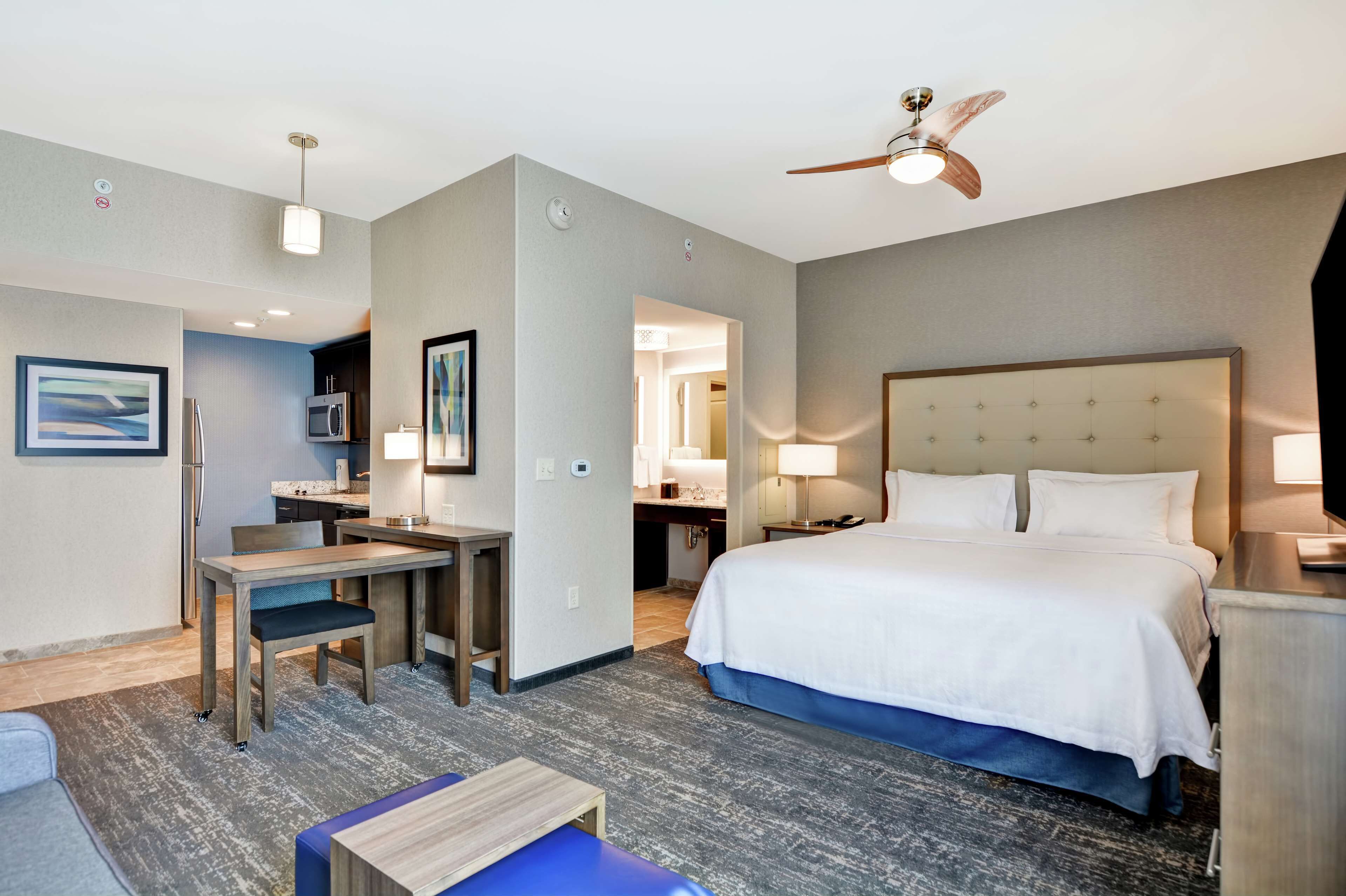 A hotel room with a bed, desk, chair, and a ceiling fan.