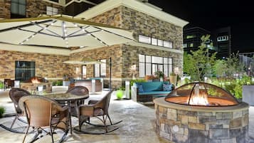 An outdoor patio area with a stone fire pit, wicker furniture, and a glass-top table.