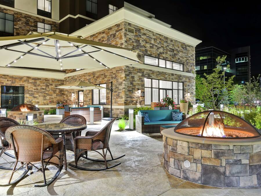 An outdoor patio area with a stone fire pit, wicker furniture, and a glass-top table.