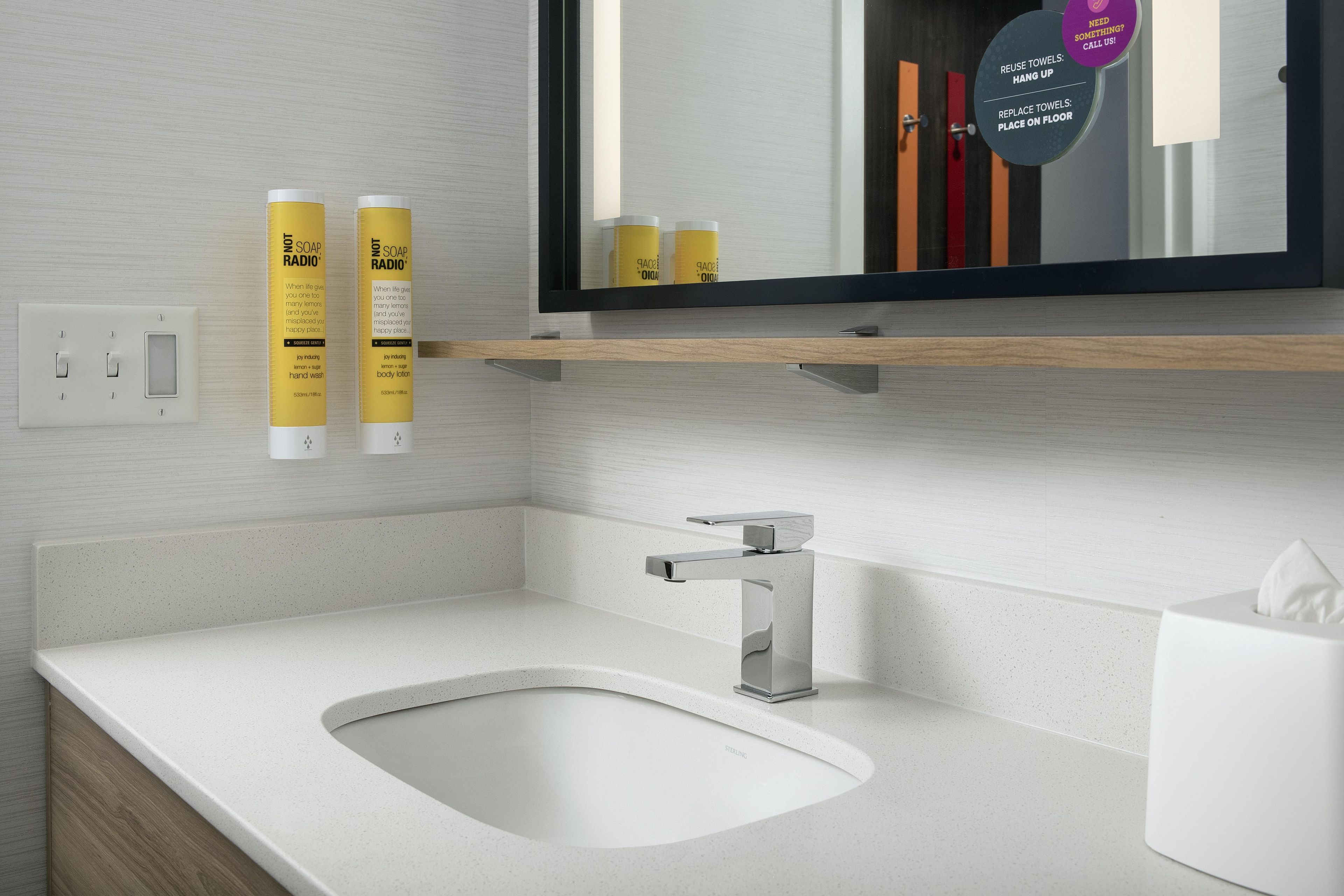 Un baño moderno con un lavamanos blanco, un espejo y dos dispensadores de jabón.