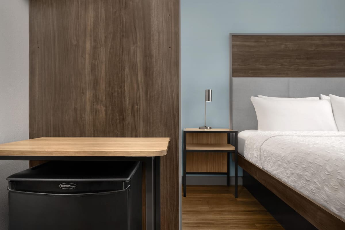 A hotel room with a bed, a nightstand, a lamp, and a trash bin.