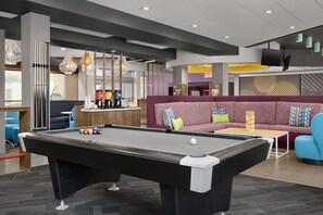 A pool table with balls, a sofa with cushions, a coffee machine, and a television mounted on the wall. - Tru by Hilton Orangeburg (Orangeburg)
