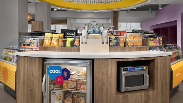 A self-service kiosk with a beverage cooler, microwave, and various food items. - Tru by Hilton Orangeburg (Orangeburg)