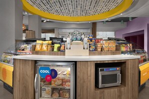 Un quiosco de autoservicio con un refrigerador de bebidas, microondas y diversos productos alimenticios.