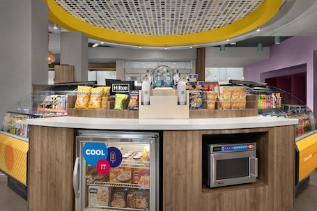 A self-service kiosk with a beverage cooler, microwave, and various food items.
