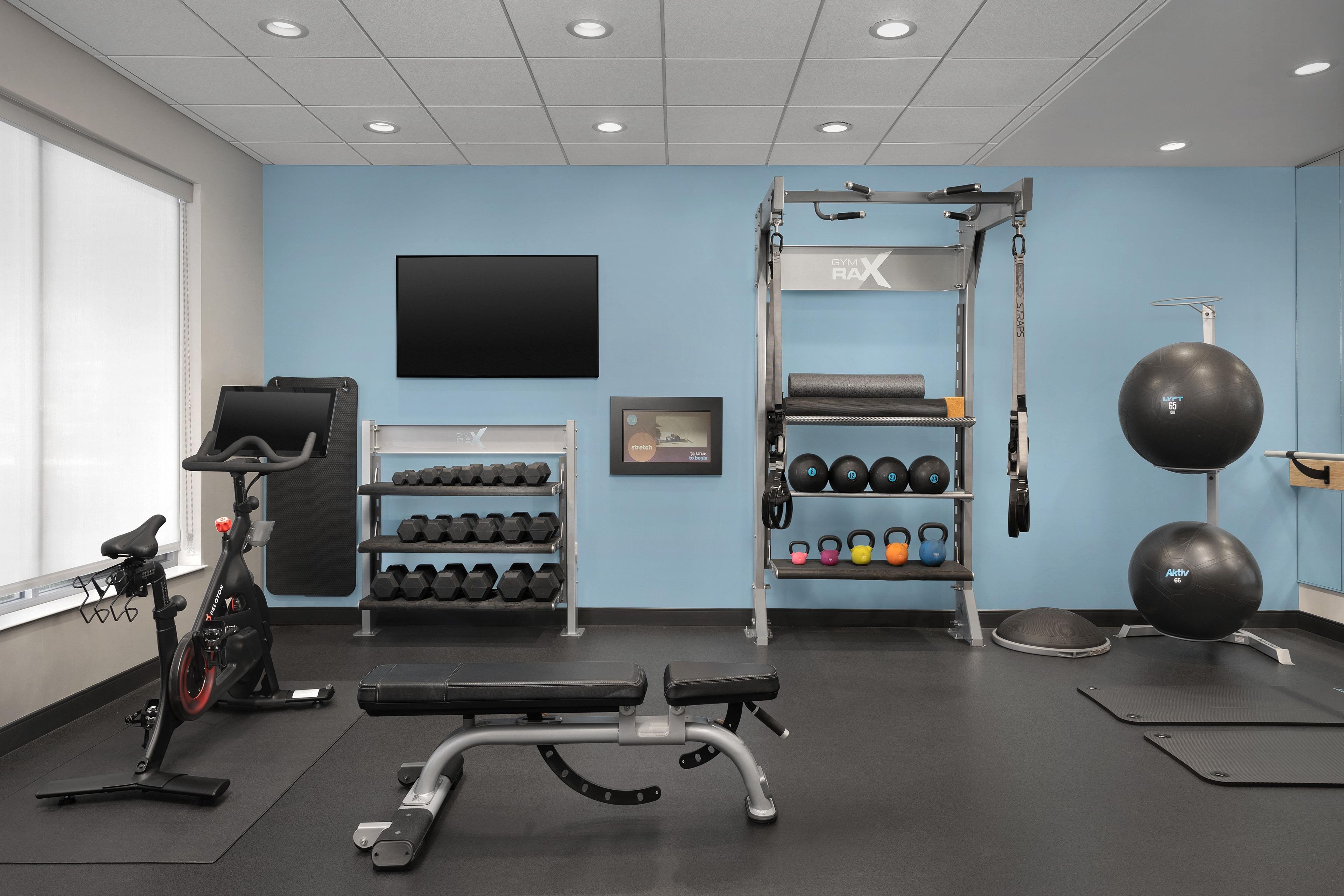 Une salle de sport équipée d’un téléviseur fixé au mur, d’haltères, de kettlebells, d’un vélo d’appartement et d’un banc.