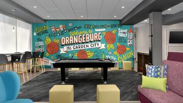 Une table de billard dans une pièce ornée d’une fresque murale aux couleurs vives, avec un canapé et des fauteuils.