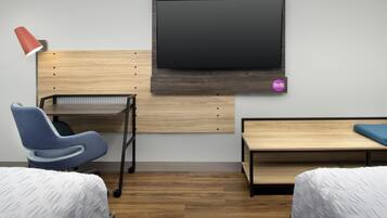 Una habitación de hotel con cama, escritorio, silla, televisor y una mesita.