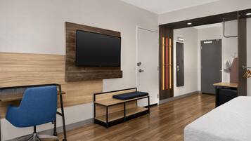 A modern hotel room with a flat-screen TV, a desk with a chair, a bed, and a wardrobe.