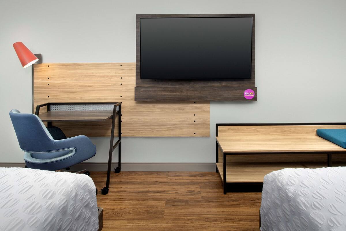 A hotel room with a wooden desk, a blue chair, a bed with white bedding, and a mounted TV.