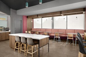 A modern cafe with a central island, seating area, and large windows. - Tru by Hilton Orangeburg (Orangeburg)
