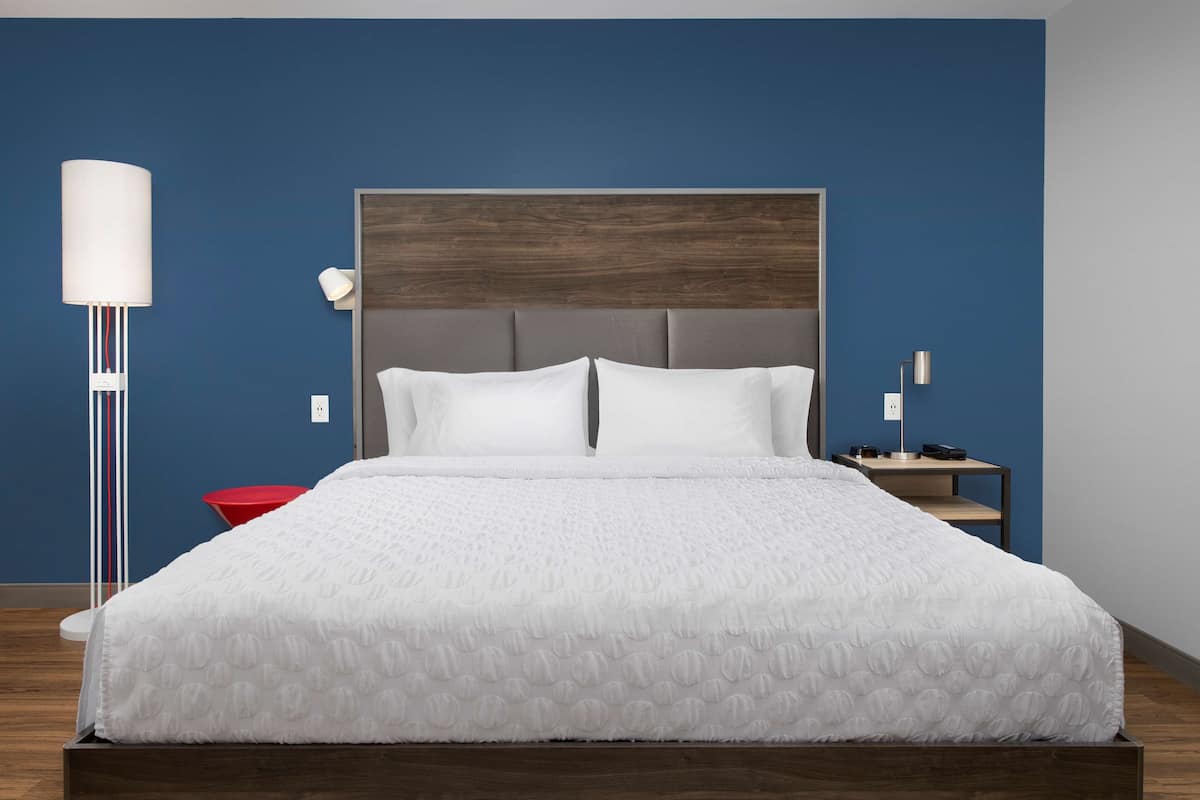 A neatly made bed with a white duvet, a modern headboard, and a bedside table with a lamp.