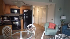 A compact kitchen with modern appliances, a dining area with a glass table, and a living space with a sofa and a lamp. - Gulf Shores Plantation ~ Resort Conference Center #1169  (Gulf Shores)