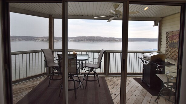 Un balcon avec vue sur un lac, un barbecue et une table avec des chaises.