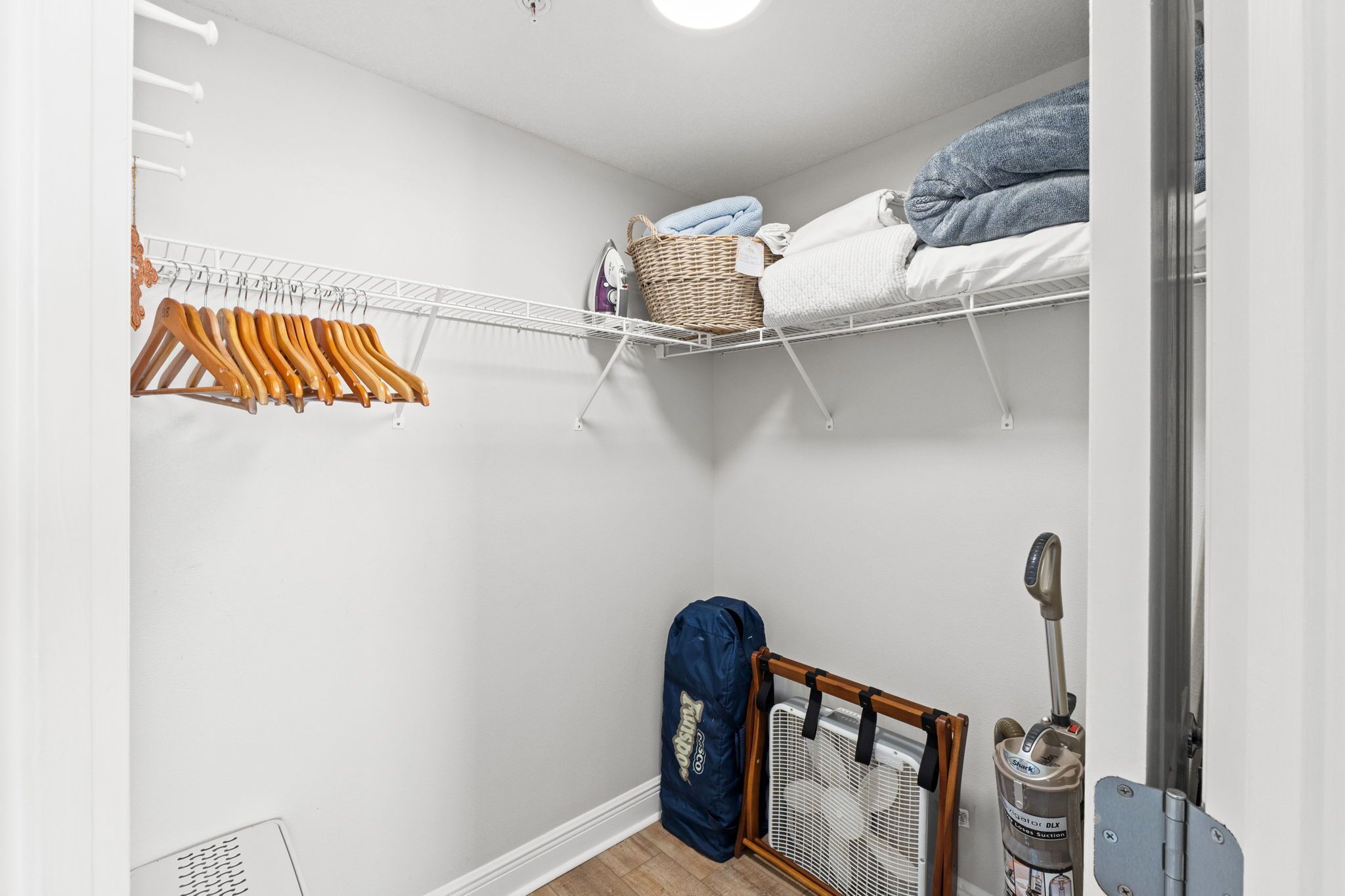 A closet with hanging clothes, a shelf with folded clothes, a basket, and a fan.