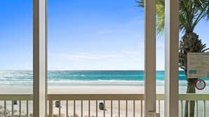 Blick auf einen Strand vom Balkon aus, mit einer Palme und einem Schild mit der Aufschrift 'Stay PCB Current'.