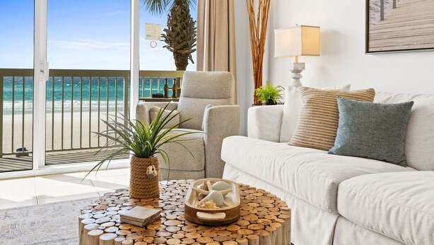 Ein Wohnzimmer direkt am Strand mit einem weißen Sofa, einem runden Couchtisch mit einem Seestern und Blick auf das Meer.