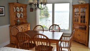 A dining room with a wooden table and chairs, a chandelier, and a view of the water. - Spectacular Waterfront Retreat Close To Portland!   (West Bath)