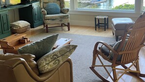 A cozy living room with a view of a lake, featuring a rocking chair, a cushioned armchair, and a wooden coffee table. - Spectacular Waterfront Retreat Close To Portland!   (West Bath)
