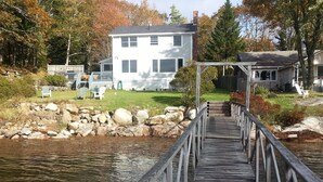 A wooden dock leading to a house with a porch, surrounded by a grassy yard and a rocky shoreline. - Spectacular Waterfront Retreat Close To Portland!   (West Bath)