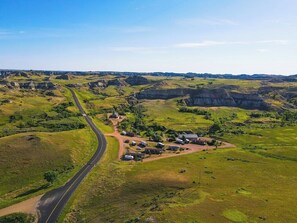 Une vue aérienne d’un paysage rural, avec une route sinueuse, des champs verdoyants et des bâtiments dispersés.