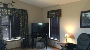 A living room with a flat-screen TV, a fireplace, a dining table, and a chair.