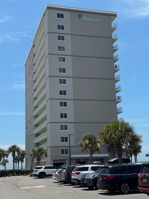 A tall hotel building with a modern design, multiple balconies, and a parking lot with several cars.