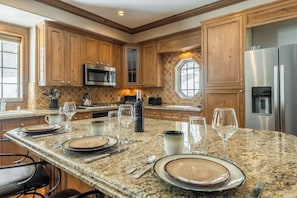 A kitchen with wooden cabinets, granite countertops, stainless steel appliances, and a dining area set for four. - Walk to Canyon Lodge | Noble Nest + Hot Tub/Sauna + 2-Car Garage (Mammoth)