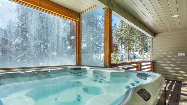 Un bain à remous dans un chalet en bois doté de grandes fenêtres.