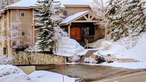 Un chalet à deux étages, avec des fondations en pierre, un revêtement extérieur en bois et un toit recouvert de neige.