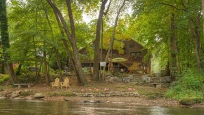 Una cabaña rústica a orillas de un río, rodeada de árboles.