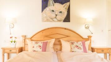 A neatly made bed with floral pillows, a wooden headboard, and a painting of a cat on the wall.