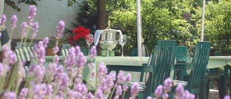 An outdoor dining area with green chairs and a table, a pitcher, and a glass of white wine.